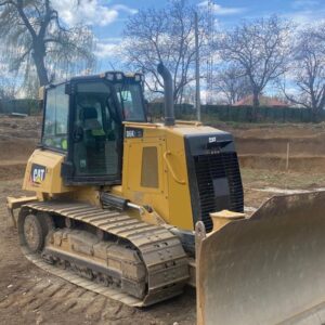 Fotografía de un tractor de orugas amarillo marca Caterpillar (CAT), modelo D6K XL, equipado con una hoja de empuje delantera, situado en un terreno de tierra en preparación bajo un cielo parcialmente nublado.