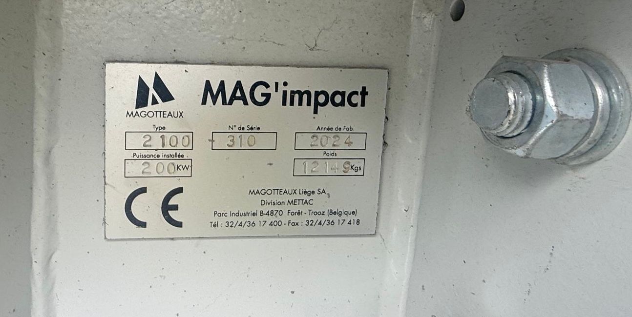 Placa de identificación metálica de una máquina MAG'impact de Magotteaux, instalada sobre una superficie metálica gris con un perno visible a la derecha, detallando especificaciones técnicas y marcado CE.